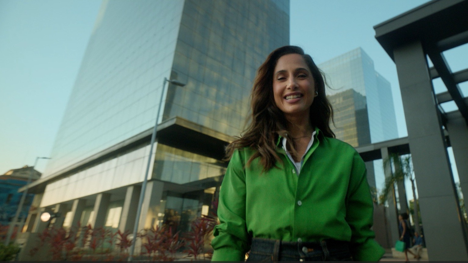 Atriz Camila Pitanga com blusa verde à frente de prédio espelhado